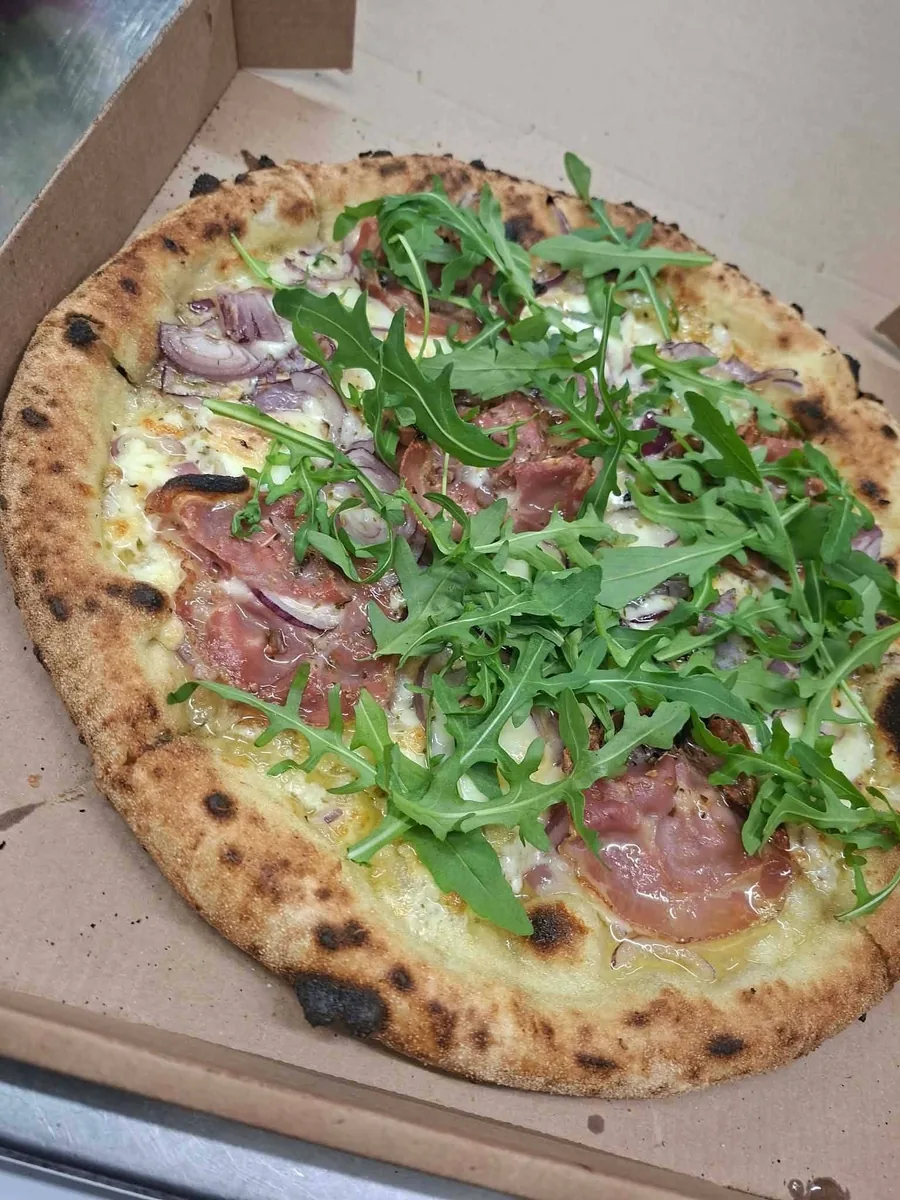Pizza au jambon cru, roquette et oignon rouge, croûte dorée